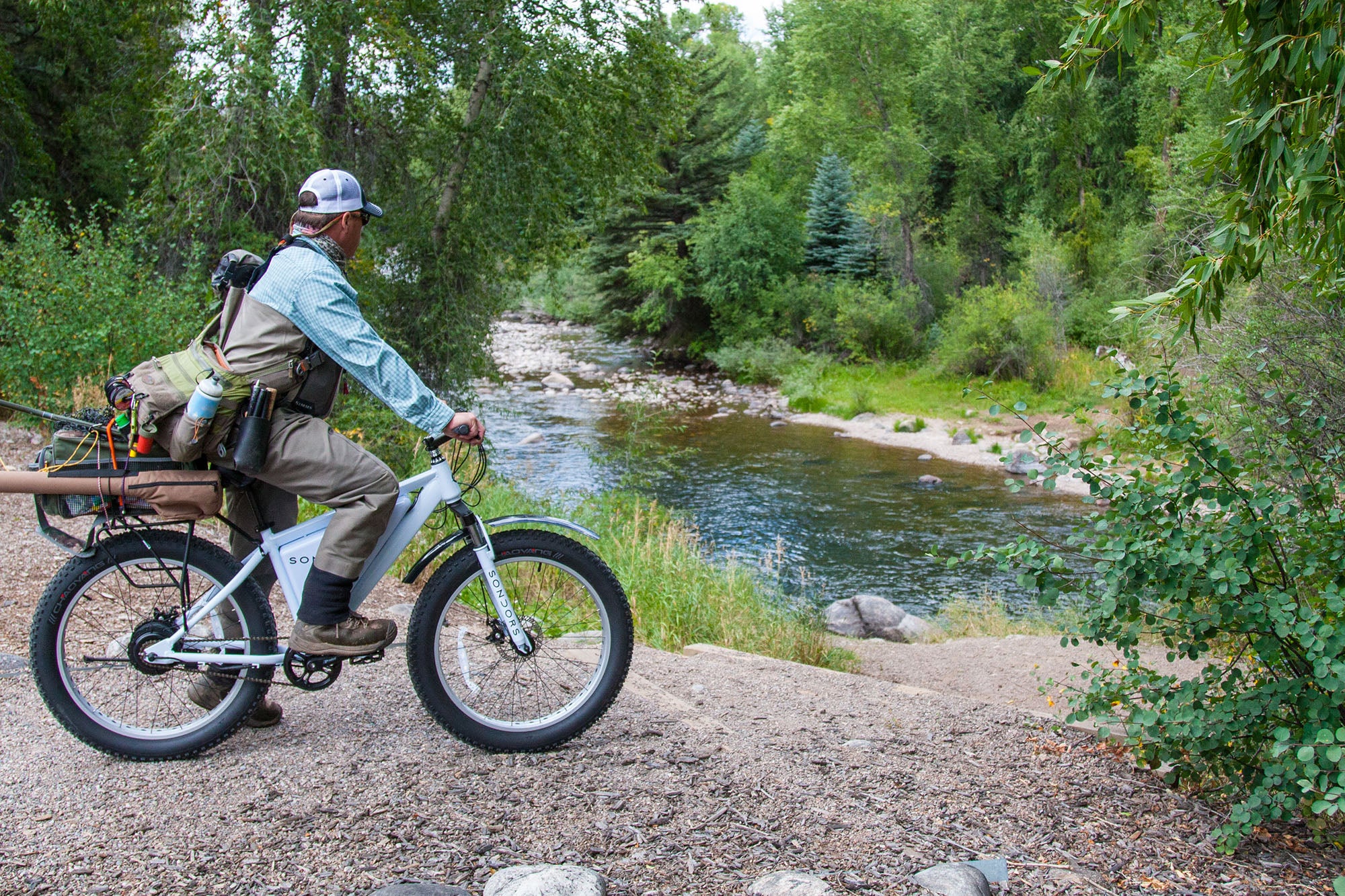 Man with a backpack riding a bike by a river in a forested area
