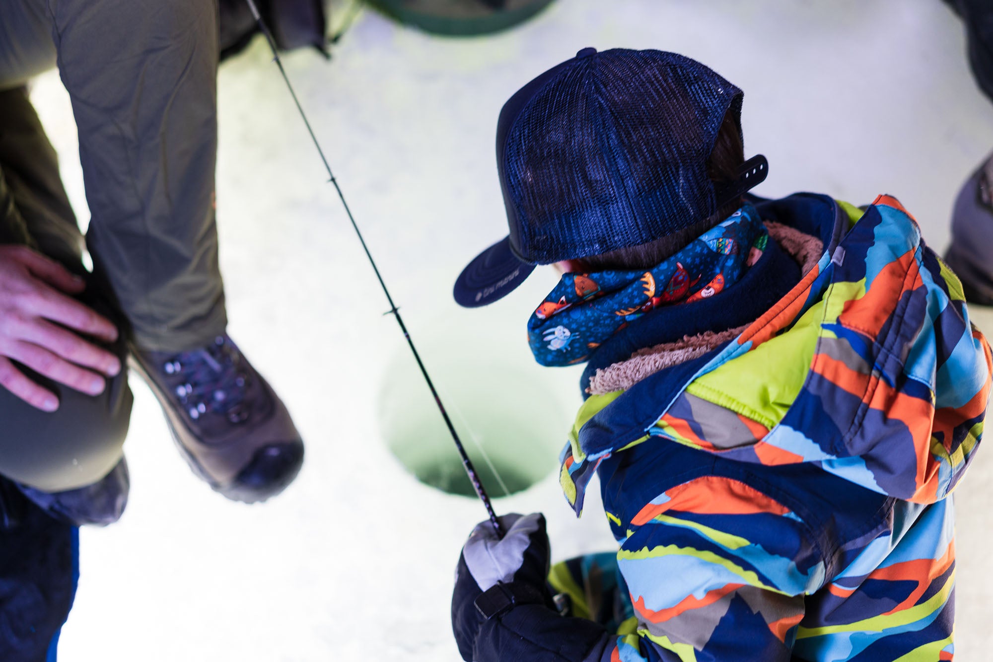 A small child ice fishing while wearing a very colorful jacket with Vail Valley Anglers at Sylvan Lake.
