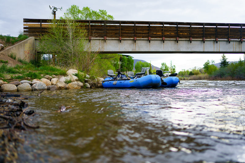 Two Vail Valley Anglers rafts on a river with a wooden bridge in the background ready for a oar certification clinic.