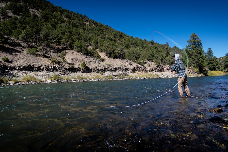 Person fly fishing in a river with a mountainous landscape in the background