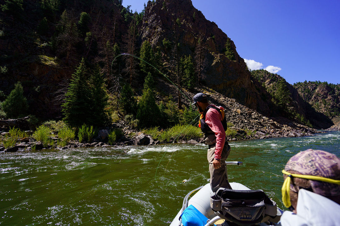 An angler hooked up with a nice fish on the Colorado River with mountains in the background.