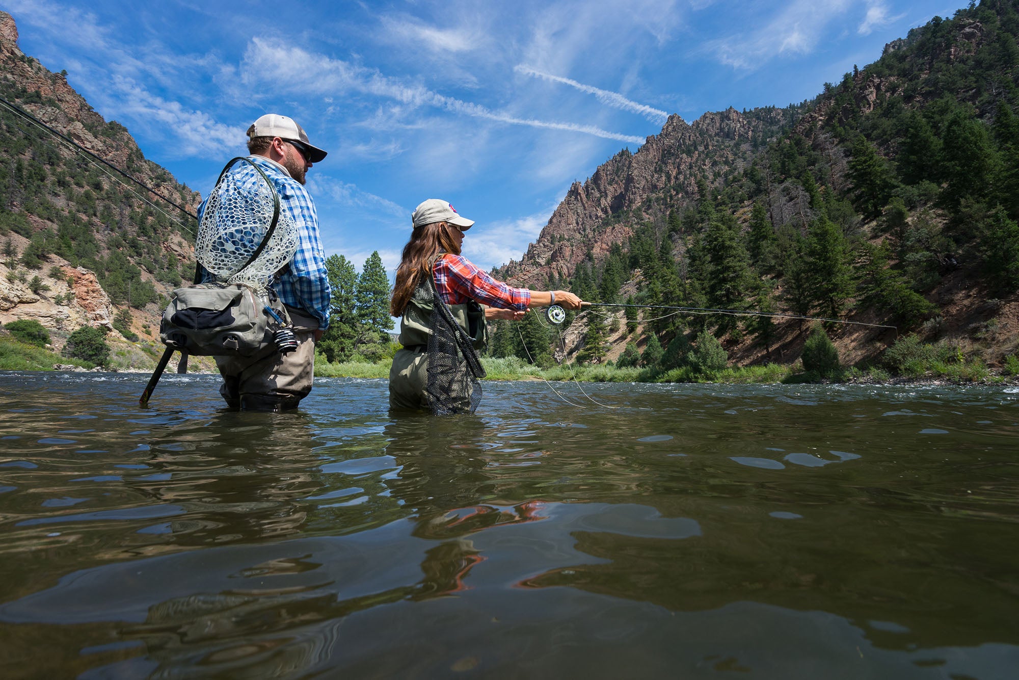 Two people fly fishing in a river with mountains in the background